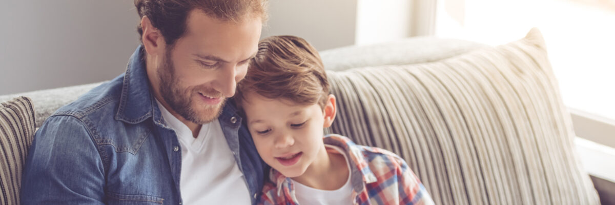 Father and son reading a book together on a sofa