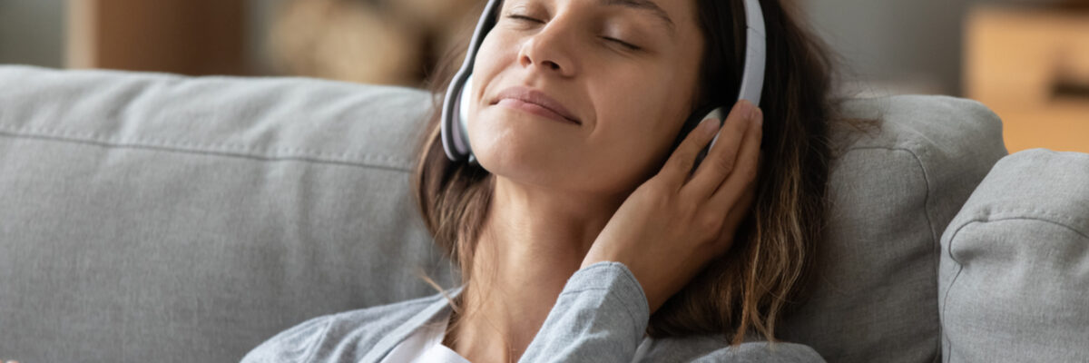 A woman wearing headphones as she sits on a sofa